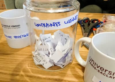 Une table en bois sur laquelle sont posé des tasses et un bocal en verre contenant des bouts de papiers griffonnés
