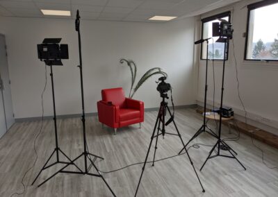 Un fauteuil rouge entouré de matériel de studio monté sur trépied (lumières, caméra...)